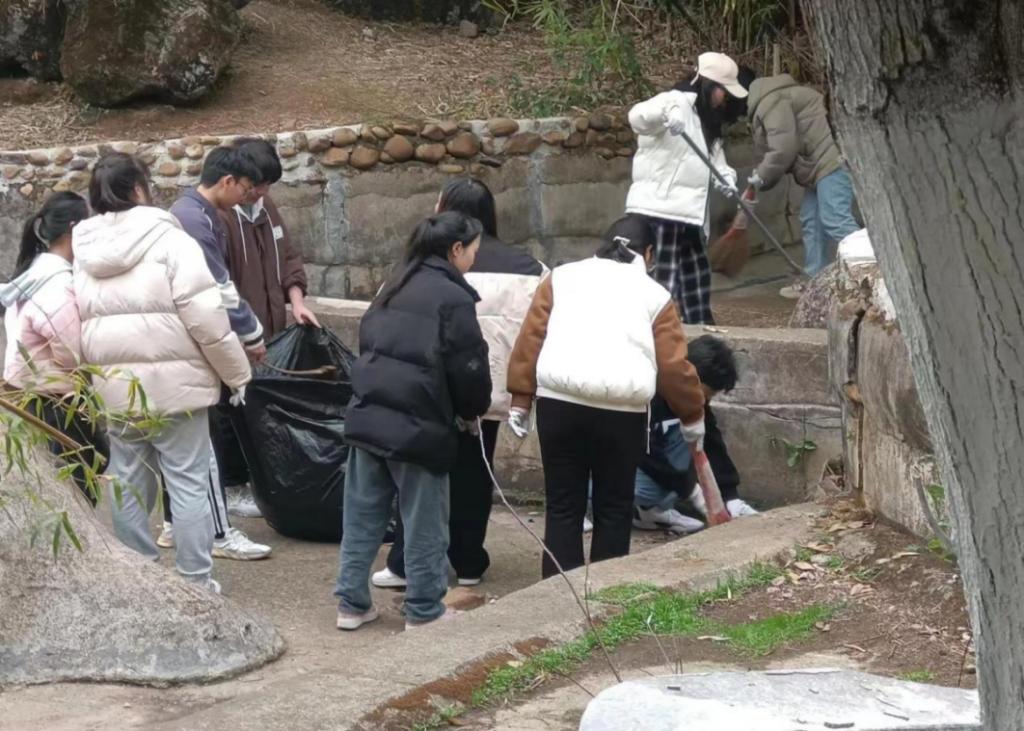 同学们合力把落叶装进垃圾袋